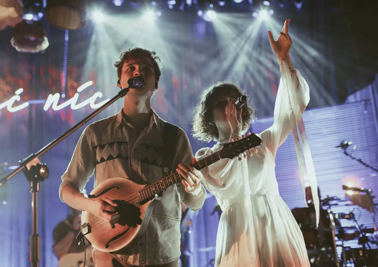 Kto śpiewa kwiat jabłoni? Młody mężczyzna gra na mandolinie, a kobieta w białej sukni śpiewa, unosząc rękę.