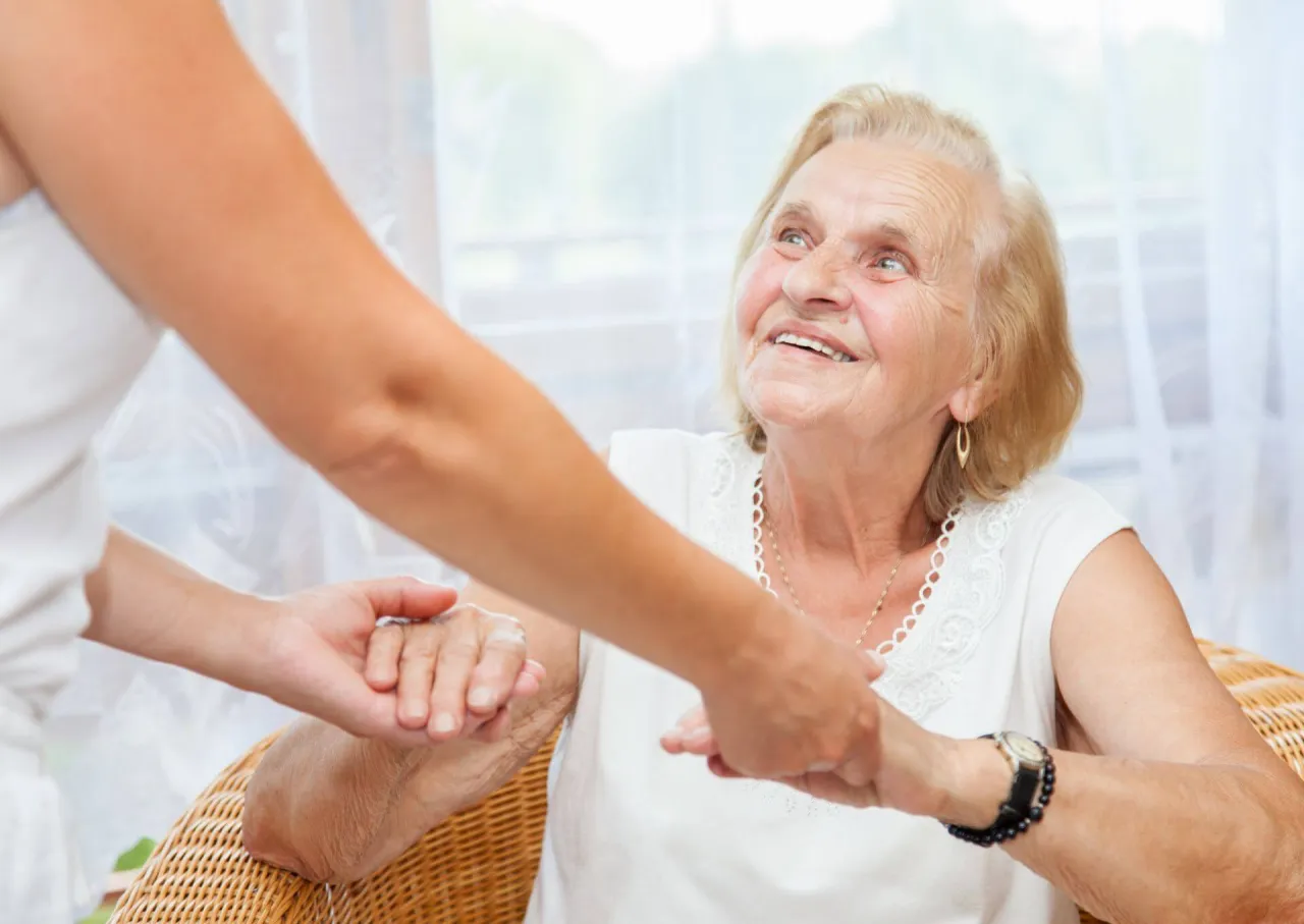 Uśmiechnięta starsza pani trzyma za rękę opiekunkę. Zastanawiasz się, ile zarabia opiekunka os&oacute;b starszych na godzinę?