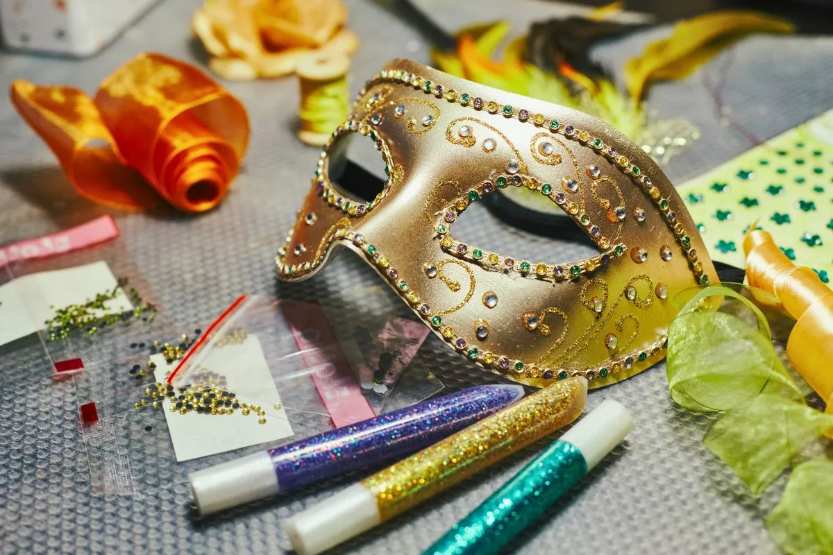 Materiały do stworzenia maski karnawałowej: złota maska, cekiny, brokatowe pisaki, wstążki. Idealne do nauki jak zrobić maskę karnawałową.