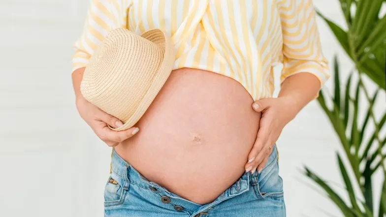 kobieta w ciąży dotyka brzucha, uśmiecha się, w tle słońce