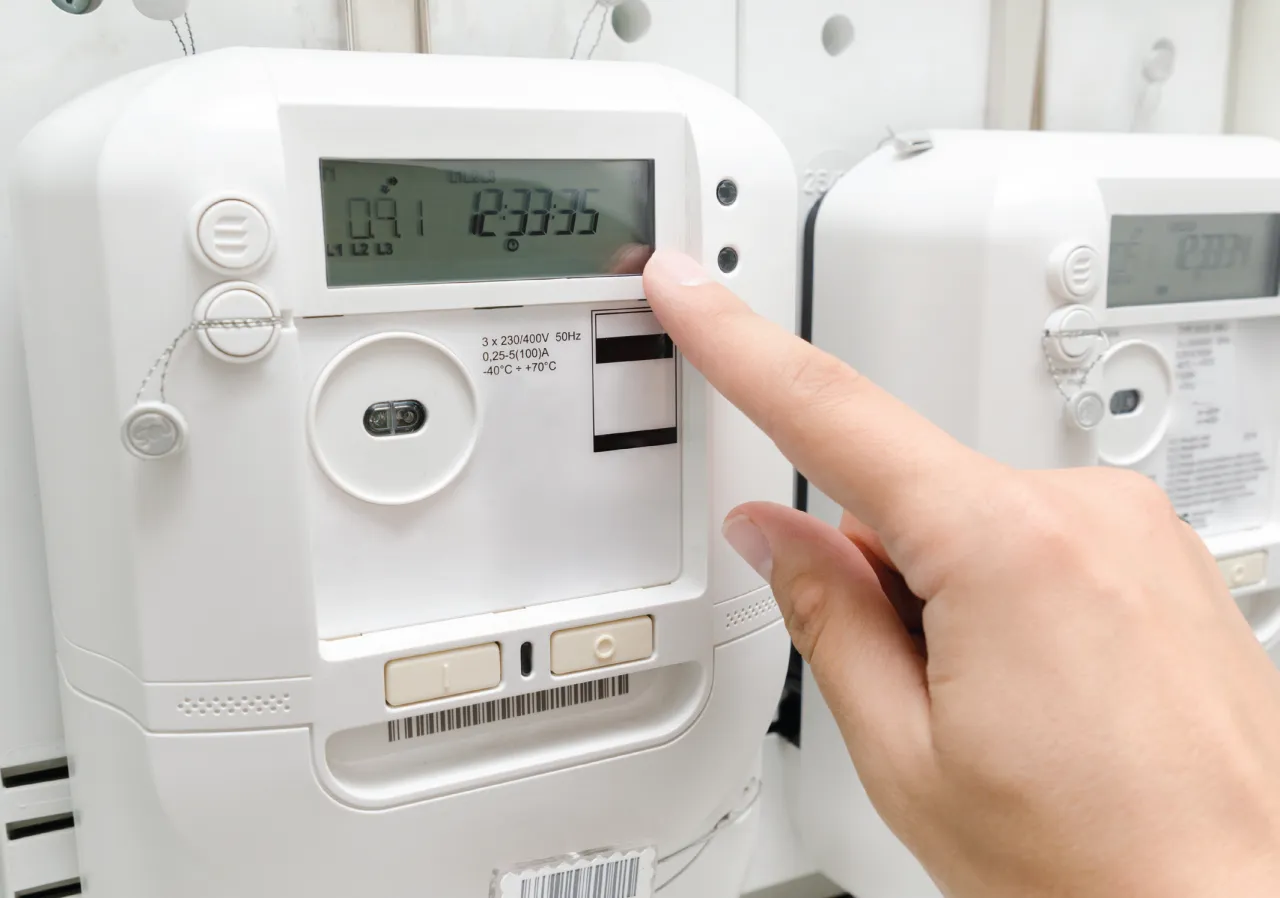Palec dotyka ekranu licznika prądu, pokazując jego aktualny stan. Obok widać kolejny licznik.