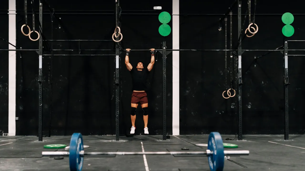 Mężczyzna wykonuje podciąganie na drążku. To element treningu crossfit, kt&oacute;ry buduje siłę i wytrzymałość.