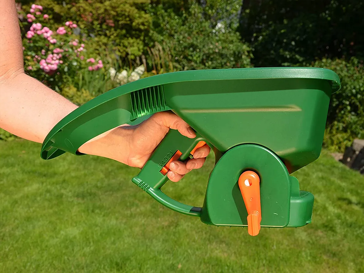 Zielony siewnik do nawozu na trawnik, trzymany w dłoni, gotowy do pracy. Idealny, by wybrać, jaki siewnik do nawozu na trawnik sprawdzi się najlepiej.