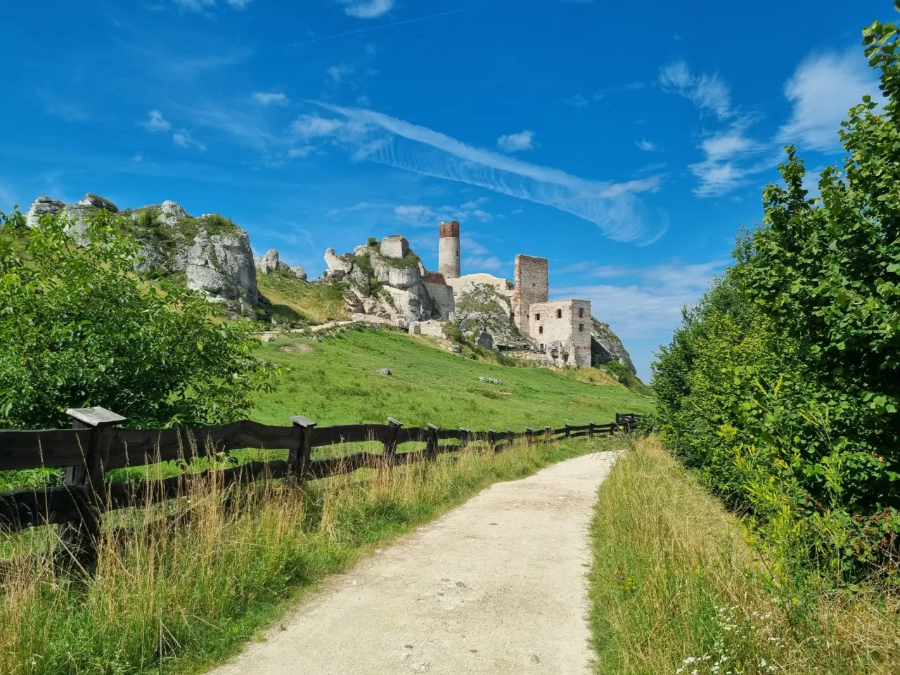 Piękny dzień na trasie rowerowej Szlak Orlich Gniazd. Ruiny zamku na wzg&oacute;rzu, zielone łąki i błękitne niebo.