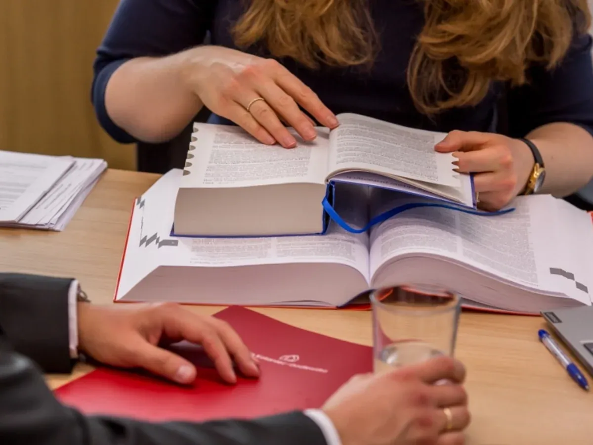 Dwie osoby analizują obszerne tomy, szukając odpowiedzi na pytanie: roszczenia co to. Na stole dokumenty, szklanka wody i długopis.