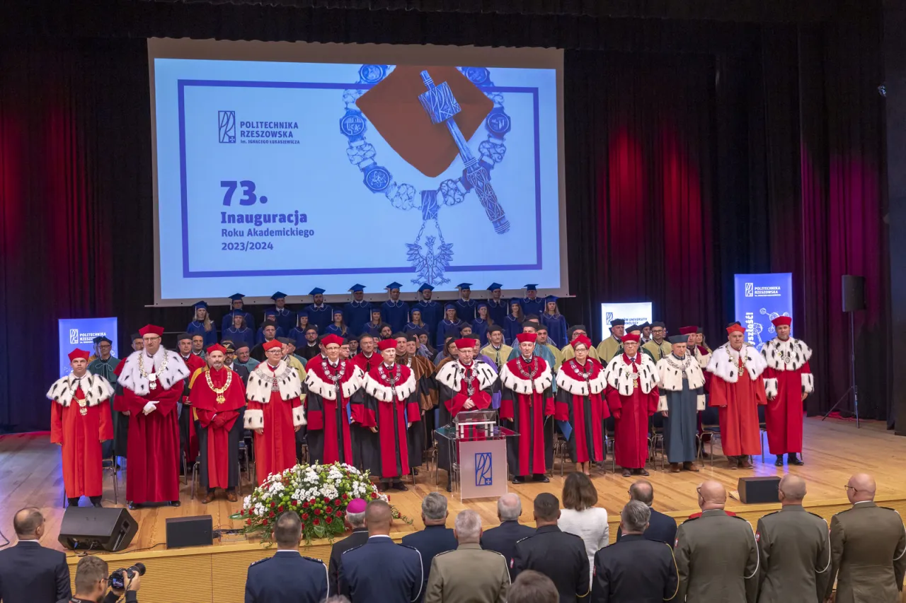 Uroczysta inauguracja roku akademickiego. Starosta w togach z innymi profesorami na scenie, podczas gdy studenci w biretach stoją za nimi.