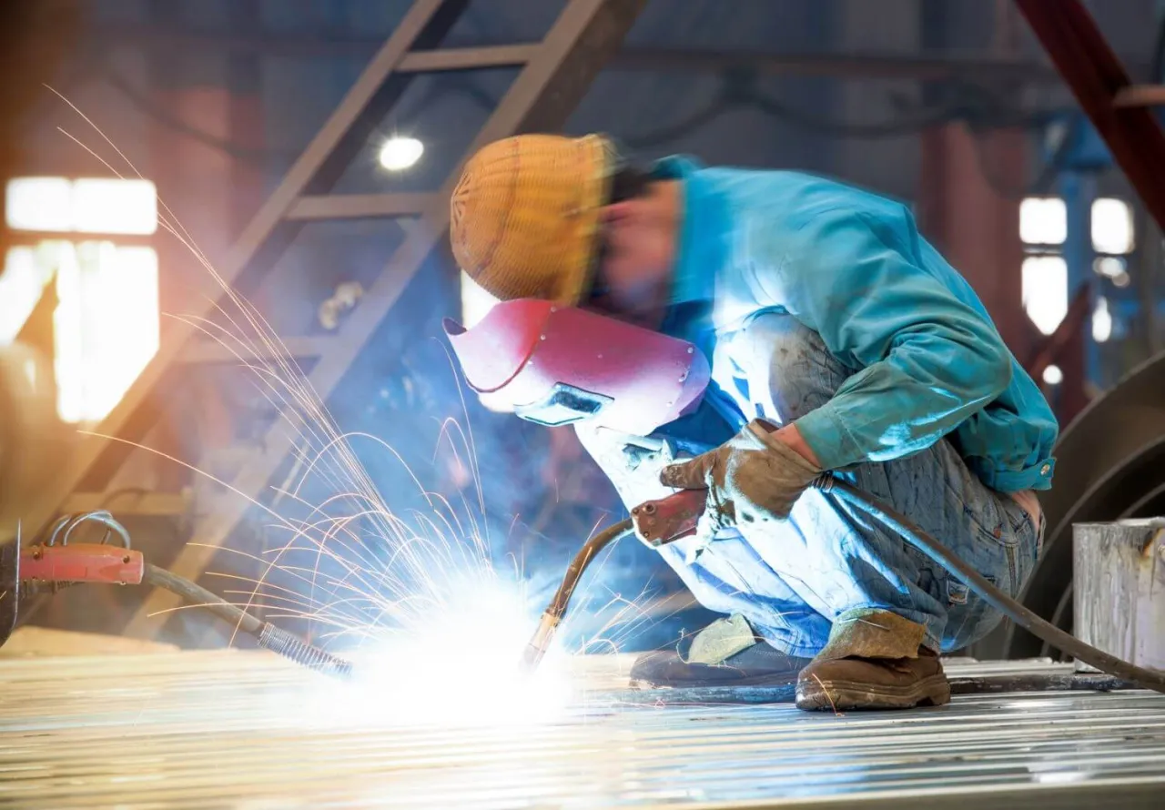 Spawacz w masce i rękawicach tworzy iskry. Zastanawiasz się, gdzie zrobić kurs spawacza? To miejsce może być początkiem Twojej kariery.