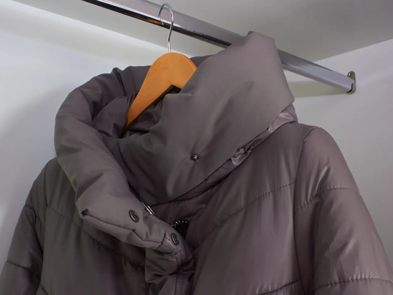 Szara, puchowa kurtka na wieszaku. Po praniu puch może się zbijać, ale jest spos&oacute;b, jak rozbić puch w kurtce po praniu, by zn&oacute;w była puszysta.