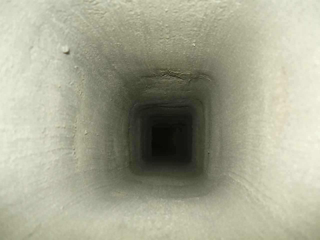 Wnętrze komina, widok z góry. Szare, pyliste ściany tworzą kwadratowy tunel. Zastanawiasz się, jak naprawić pęknięty komin?
