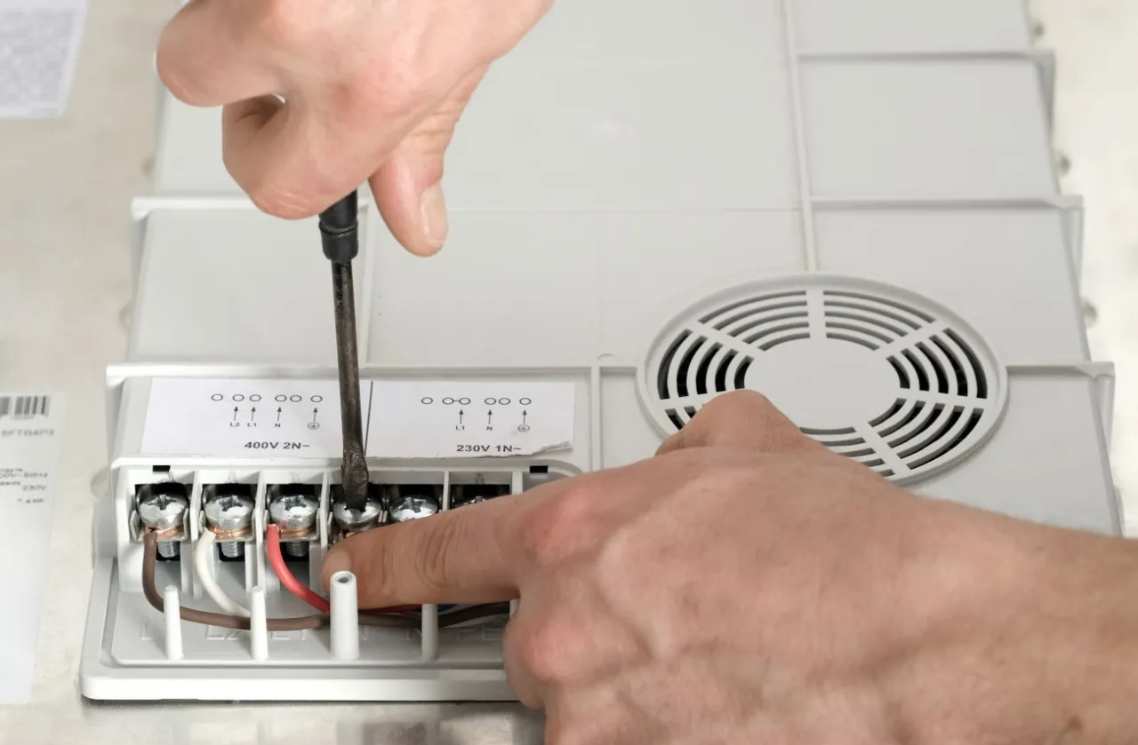 Ręce przykręcają przewód do płyty indukcyjnej. Widać śrubokręt i zaciski elektryczne.