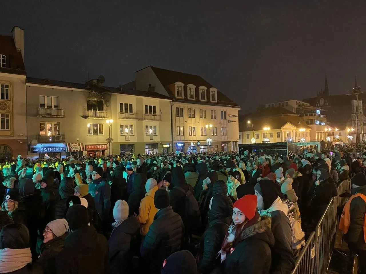 Tłum ludzi świętuje sylwester w Białymstoku. Widać budynki, światła i scenę.