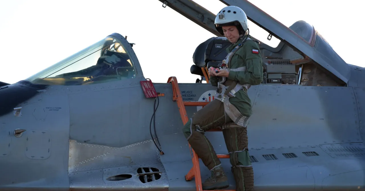 Kobieta w kombinezonie pilota, z hełmem na głowie, schodzi po drabinie z myśliwca. Wygląda jak żona Hołowni, która została pilotem.