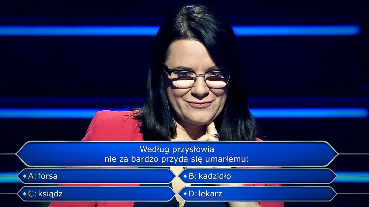 Kobieta w okularach na tle niebieskich pas&oacute;w, zastanawia się nad pytaniem z teleturnieju 