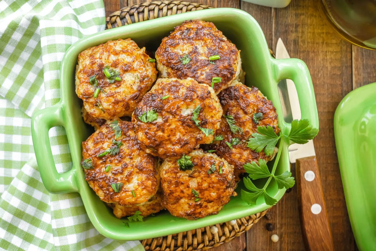 Złociste kotlety mielone wieprzowe lub drobiowe, posypane natką pietruszki, w zielonej misce.