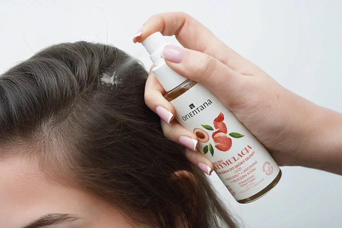 Dłoń aplikuje wcierkę do włos&oacute;w Orientana na sk&oacute;rę głowy. To produkt, kt&oacute;rego nie trzeba spłukiwać, by pobudzić wzrost włos&oacute;w.