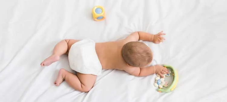 niemowlę leżące na brzuszku i sięgające po kolorową zabawkę