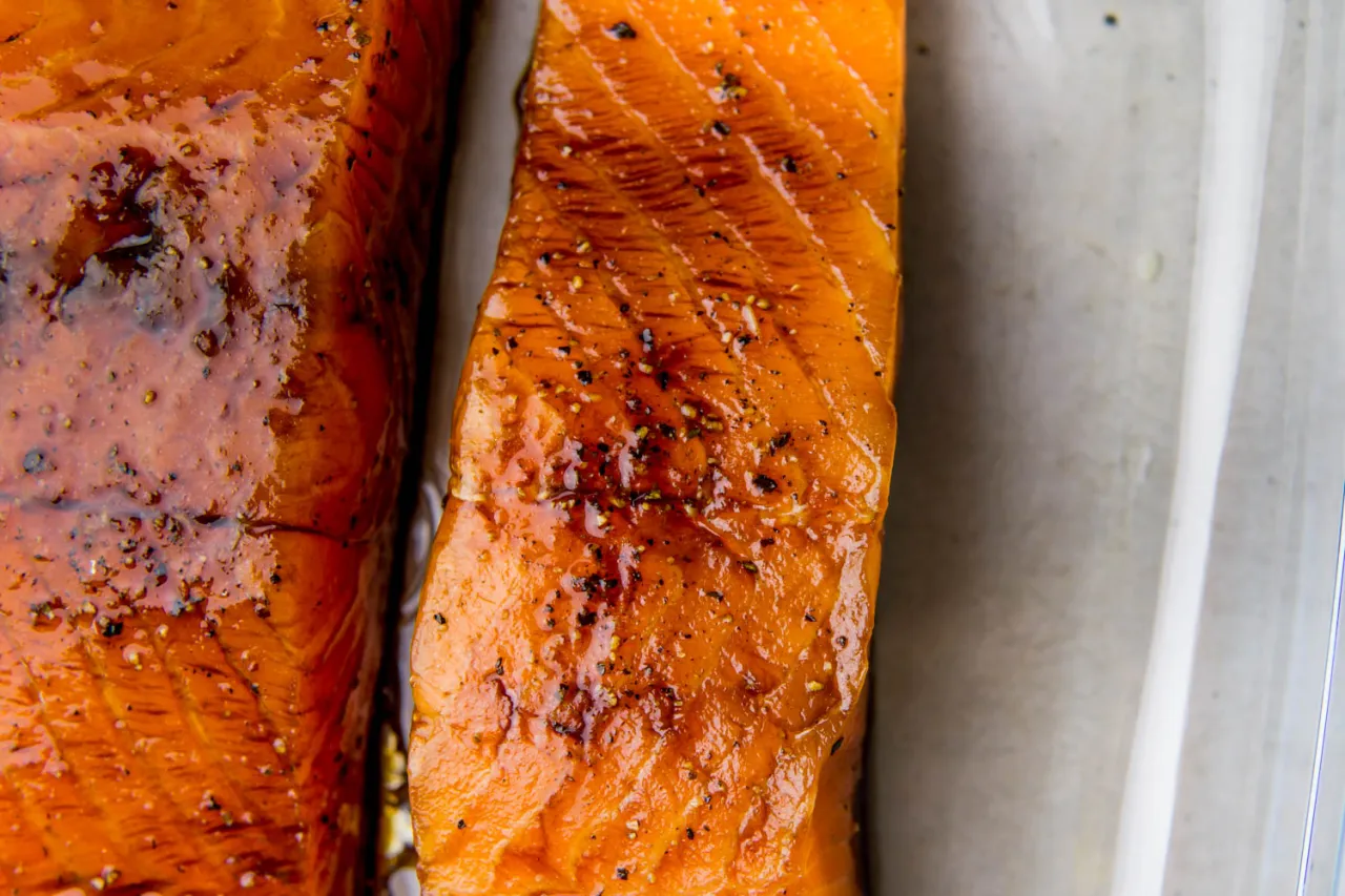 Dwa soczyste kawałki łososia w sosie sojowym, błyszczące i doprawione pieprzem, gotowe do podania.