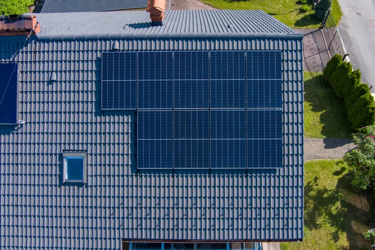 Panele fotowoltaiczne na dachu domu, czerpiące czystą energię słoneczną. Obok małe okienko dachowe i komin.