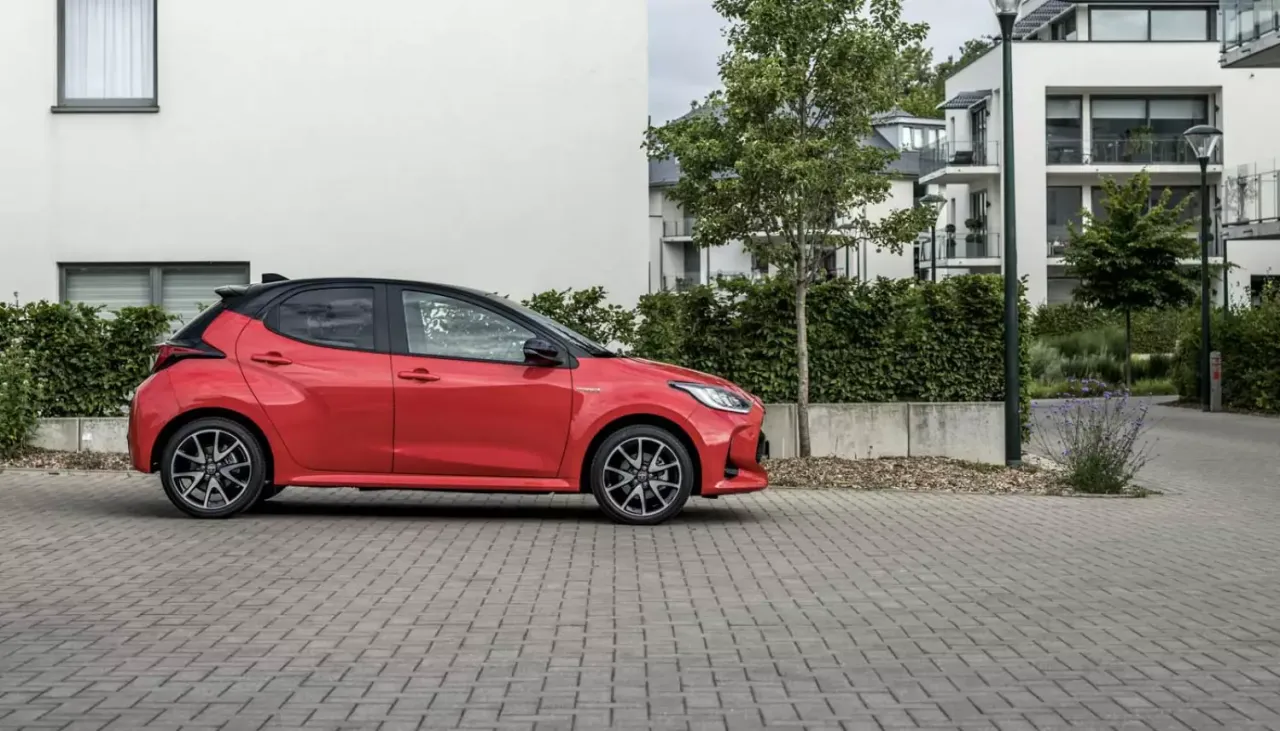 Czerwony, sportowy samoch&oacute;d, idealne pierwsze auto dla dziewczyny, zaparkowany przed nowoczesnym budynkiem.