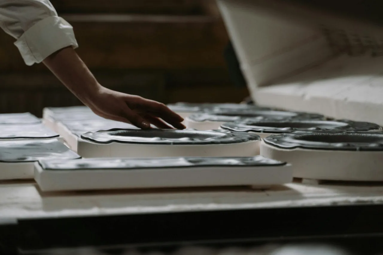 Dłoń dotyka czarnych, falistych naczyń w pracowni muzeum sztuk użytkowych.