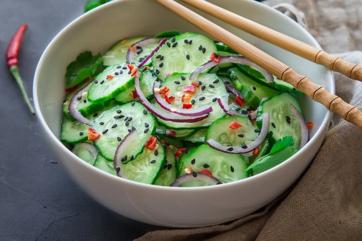 Chrupiące og&oacute;rki po tajsku z czerwoną cebulą, chili i czarnym sezamem, gotowe do podania z pałeczkami.
