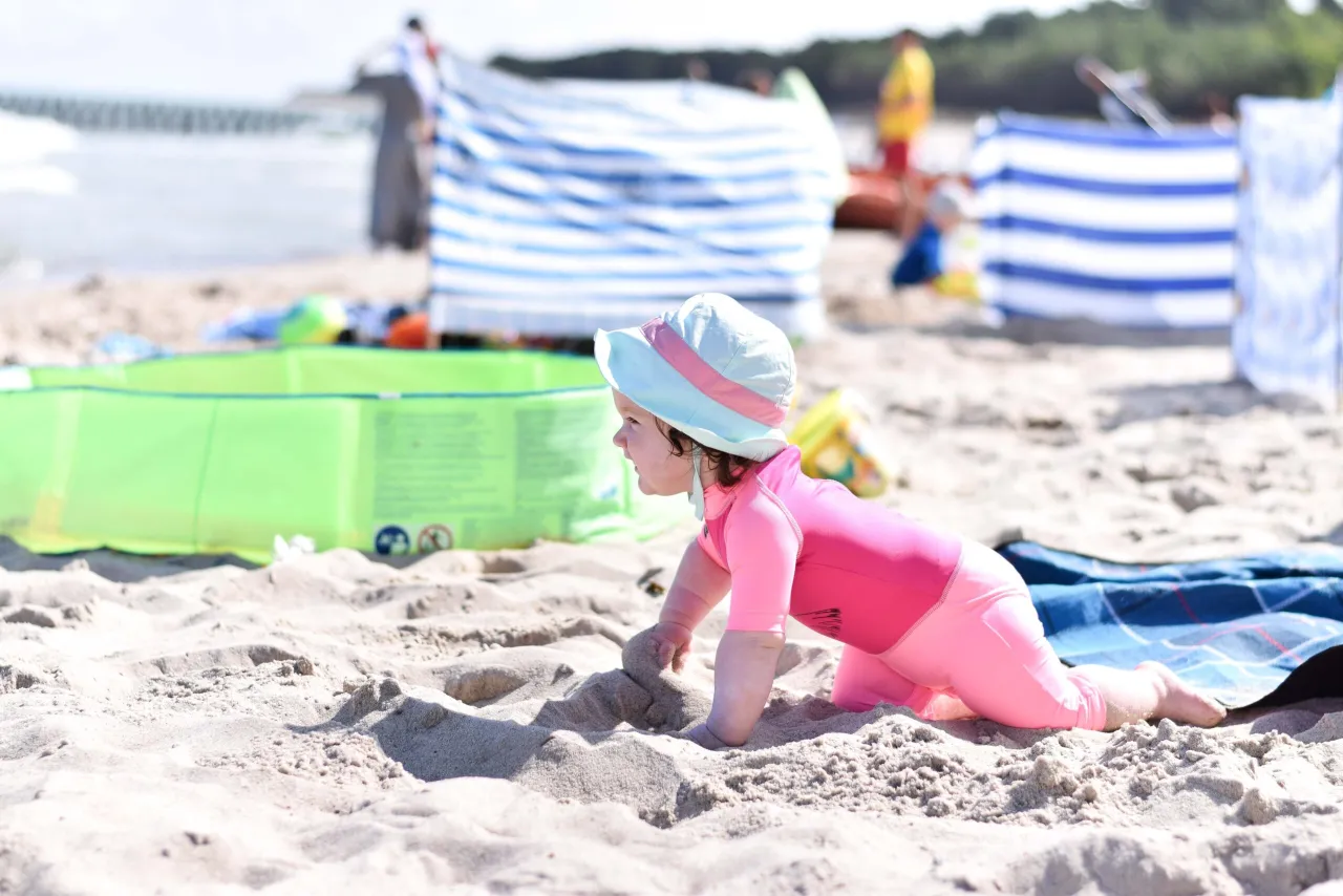 Małe dziecko w różowym stroju kąpielowym i kapelusiku odkrywa piasek na plaży. To idealny dzień, kiedy jod nad morzem działa cuda.