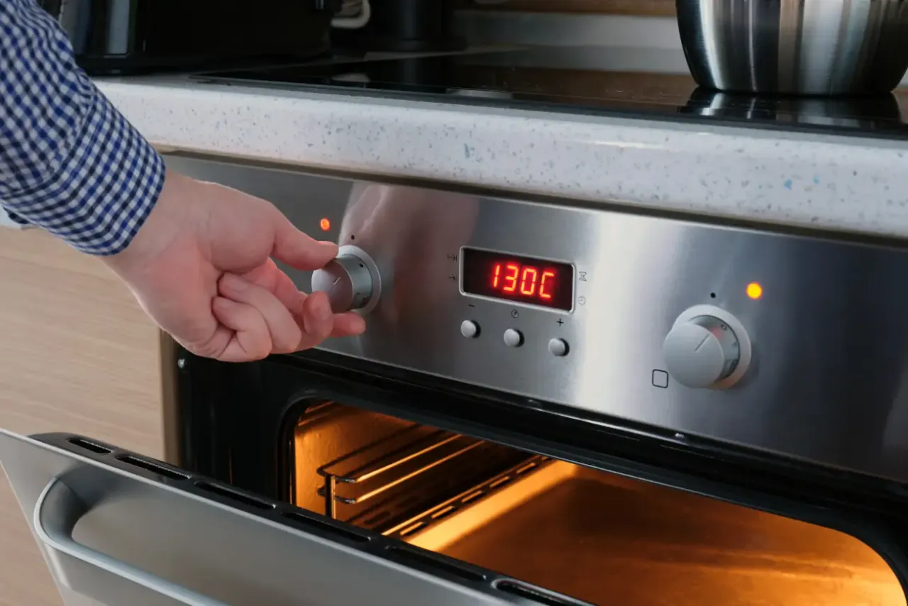 Ręka kręci pokrętłem piekarnika, ustawiając temperaturę 130°C do pasteryzowania w piekarniku.
