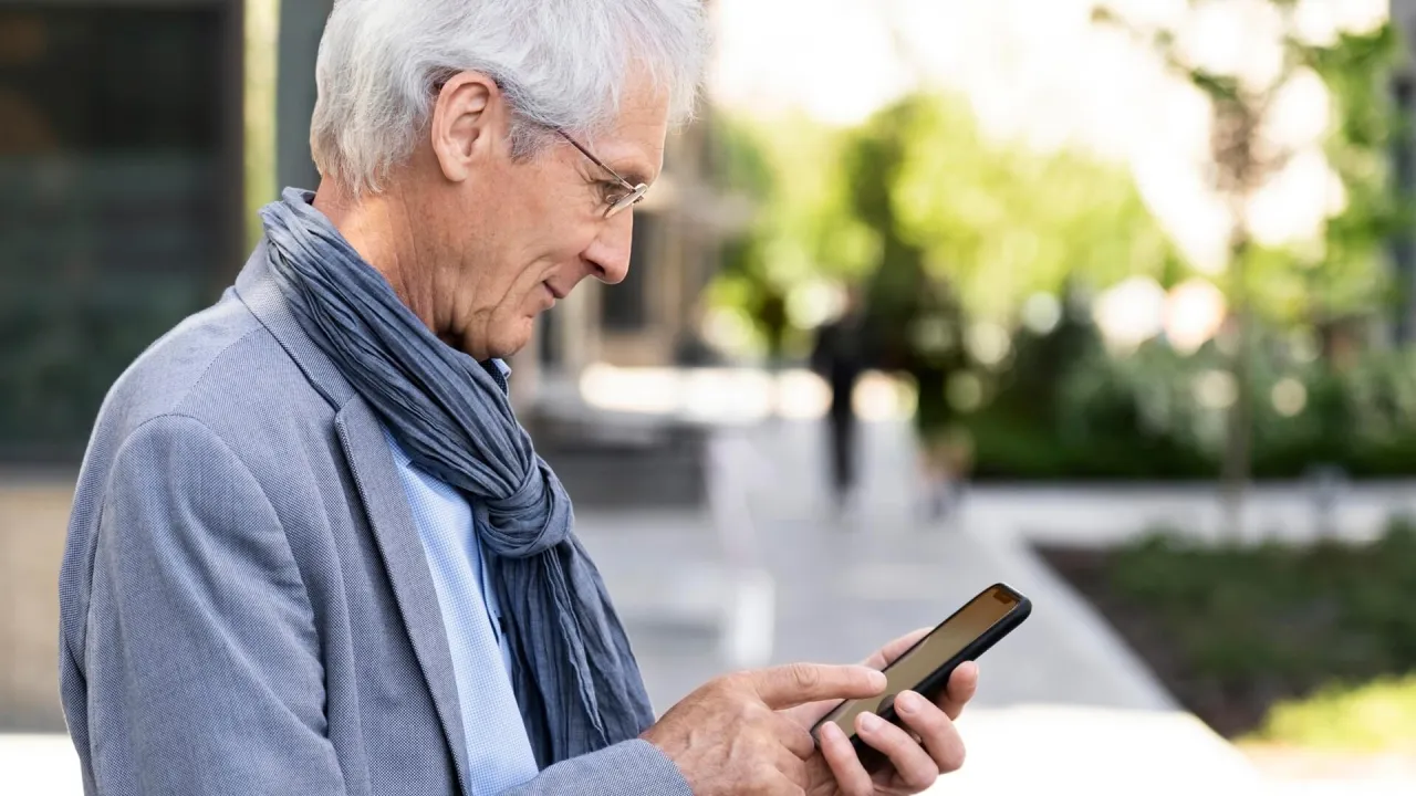 Starszy mężczyzna z aparatem słuchowym Signia uczy się, jak sparować go z telefonem, korzystając z instrukcji na ekranie.