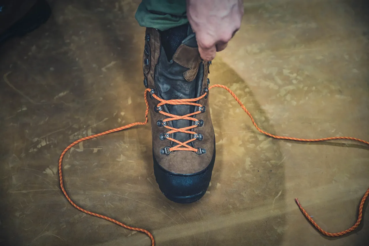 Dłoń sznuruje brązowy but za kostkę pomarańczowym sznurówką. Pokazano, jak sznurować buty za kostkę.