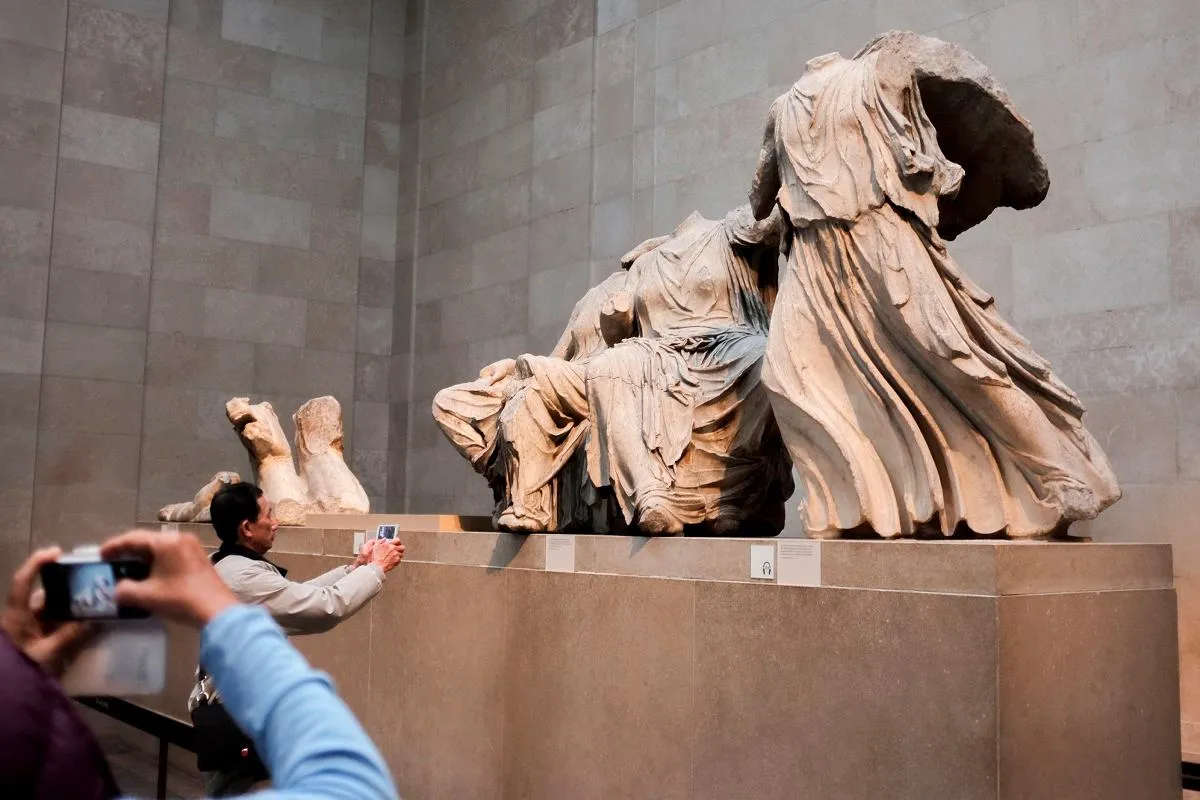 Trzy fragmenty rzeźb, prawdopodobnie trzy mojry Fidiasza, w muzeum. Ludzie robią im zdjęcia.