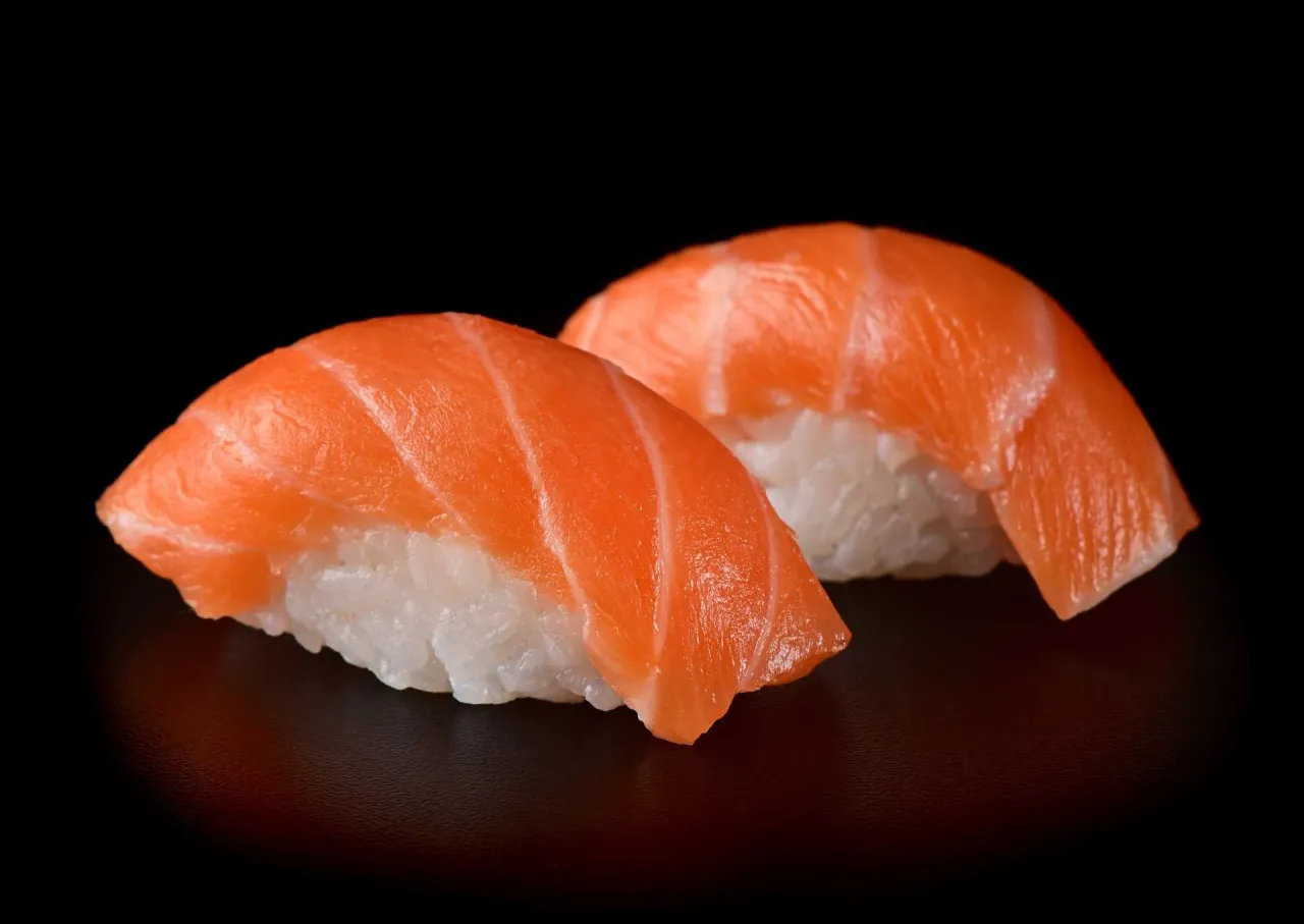 Dwa kawałki sushi z łososiem na czarnym tle. Czy sushi można zamrozic? Zazwyczaj nie, ale ten łosoś wygląda świeżo.