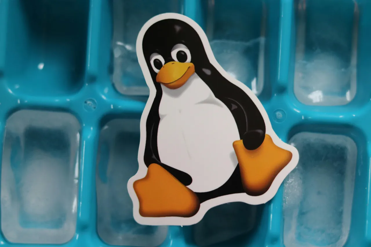 Tux, maskotka jądra Linux, siedzi na niebieskiej tacce z kostkami lodu.
