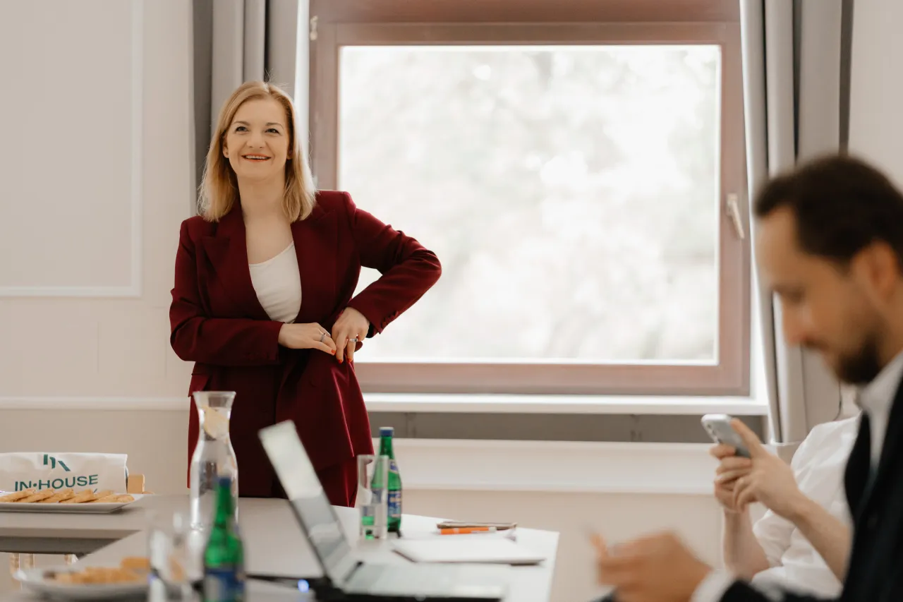 Uśmiechnięta kobieta w garniturze opowiada o tym, jak zostać prawnikiem bez aplikacji. Na stole laptop i ciasteczka.