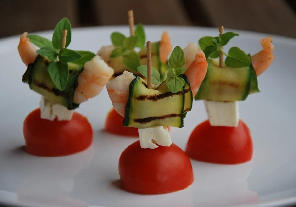 Apetyczne koreczki z krewetkami, cukinią, fetą i pomidorkami koktajlowymi, ozdobione świeżą bazylią.