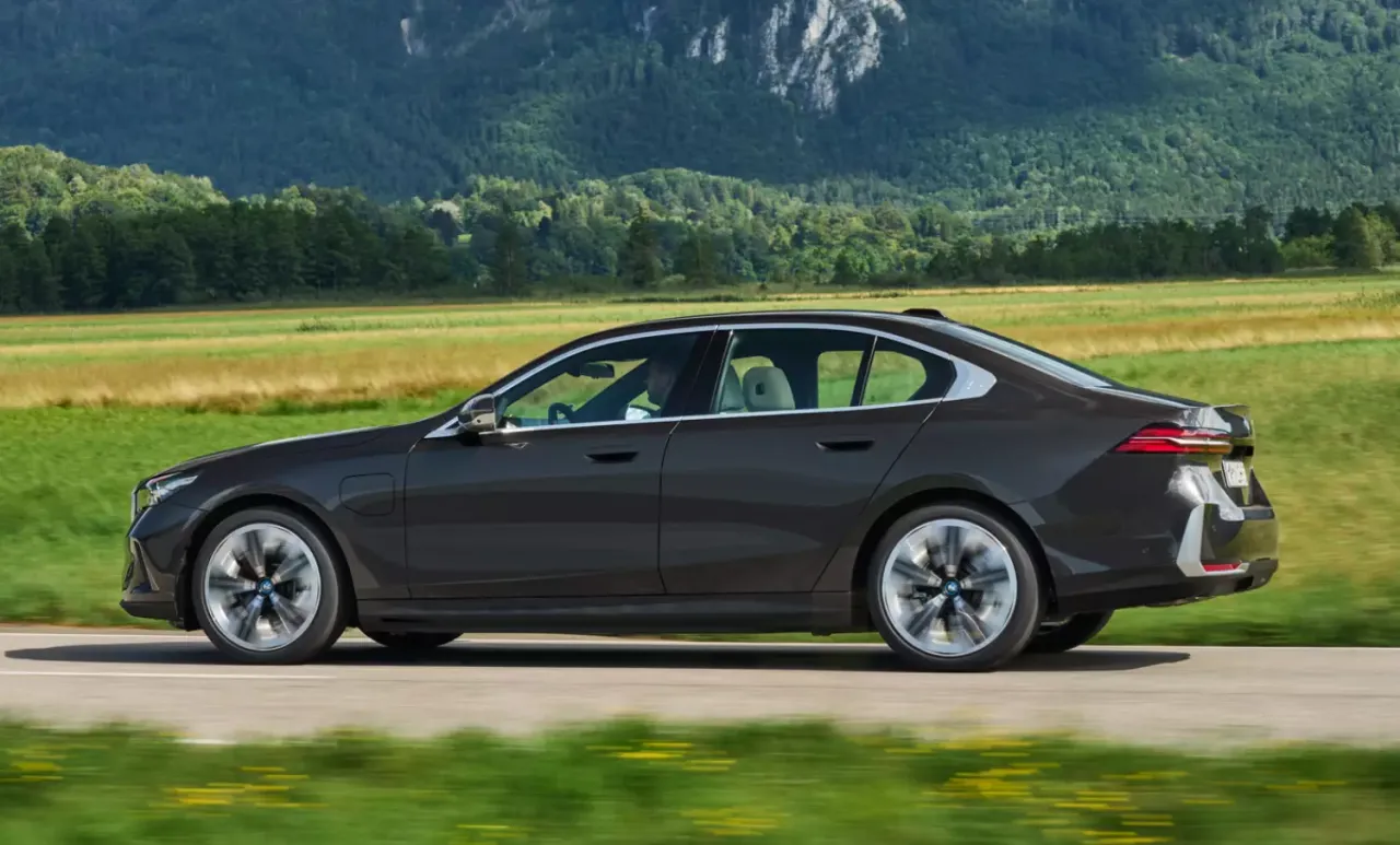 Ciemnoszary sedan jedzie drogą wśród zielonych pól i gór. Idealny na leasing do 150 tys.