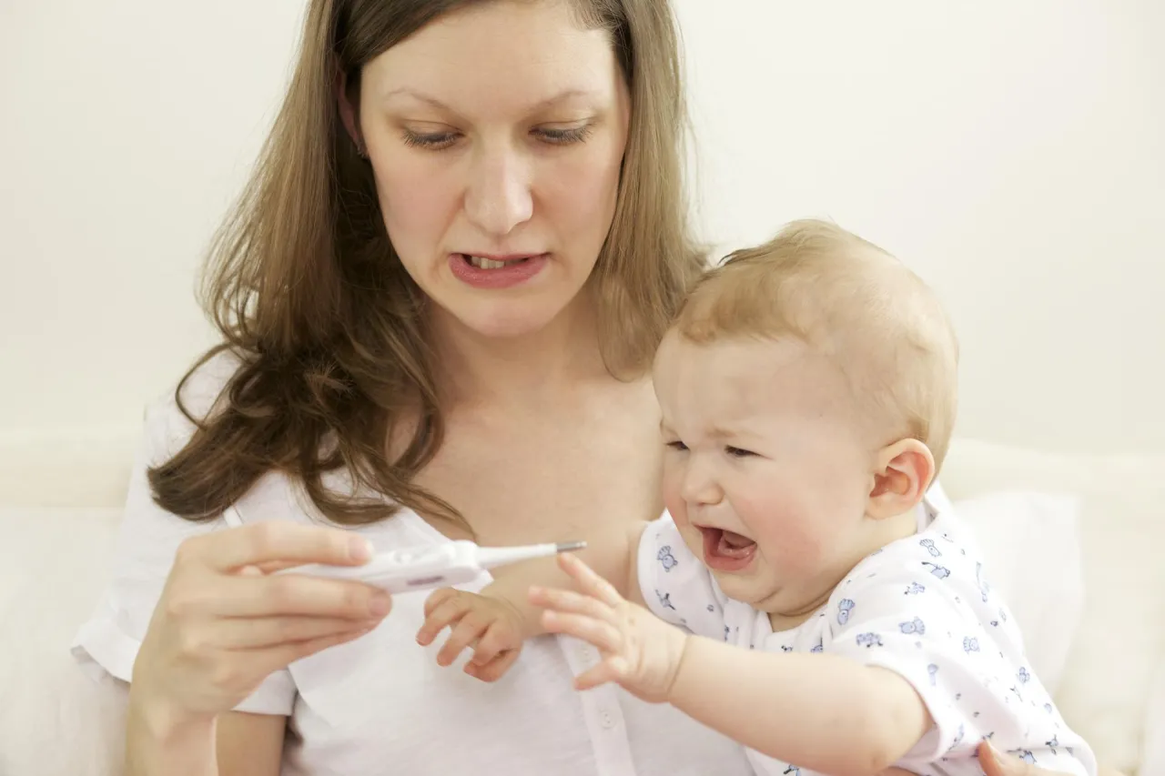 kobieta trzymająca się za bolącą głowę po szczepieniu, z termometrem