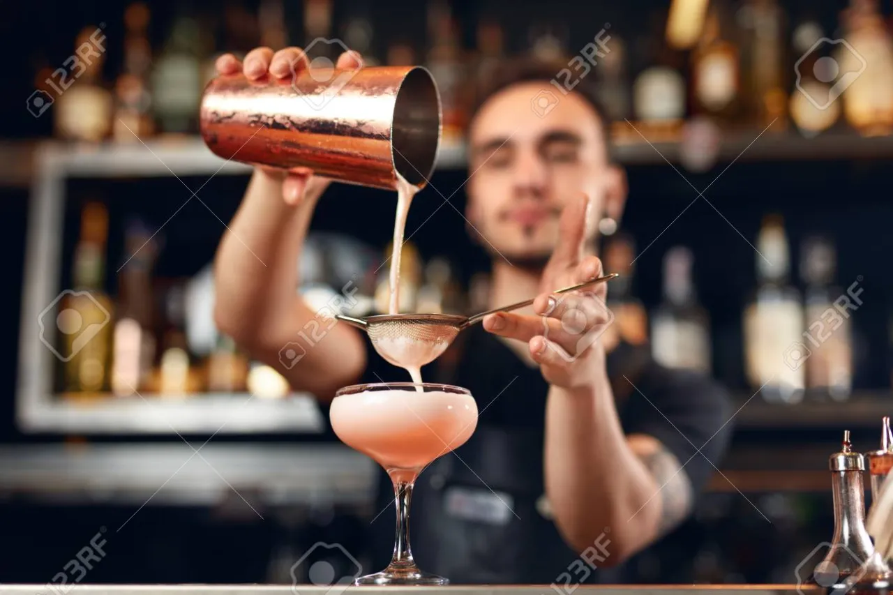 Barman nalewający drinka do szklanki używając jiggera