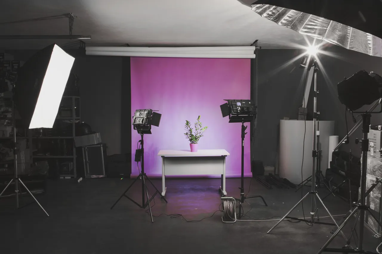 Studio do sesji produktowej. Różowe tło, biurko z rośliną, lampy studyjne. Idealne miejsce, by dowiedzieć się, jak zrobić zdjęcie produktu.