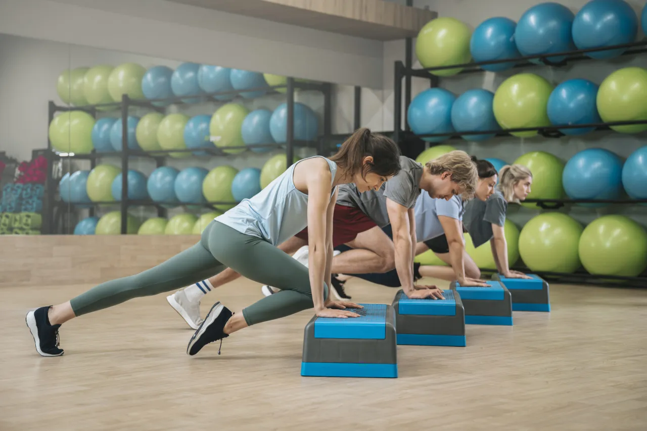 Grupa osób ćwiczy w pozycji deski na stepach. Intensywny trening, który może być częścią sesji tabata.