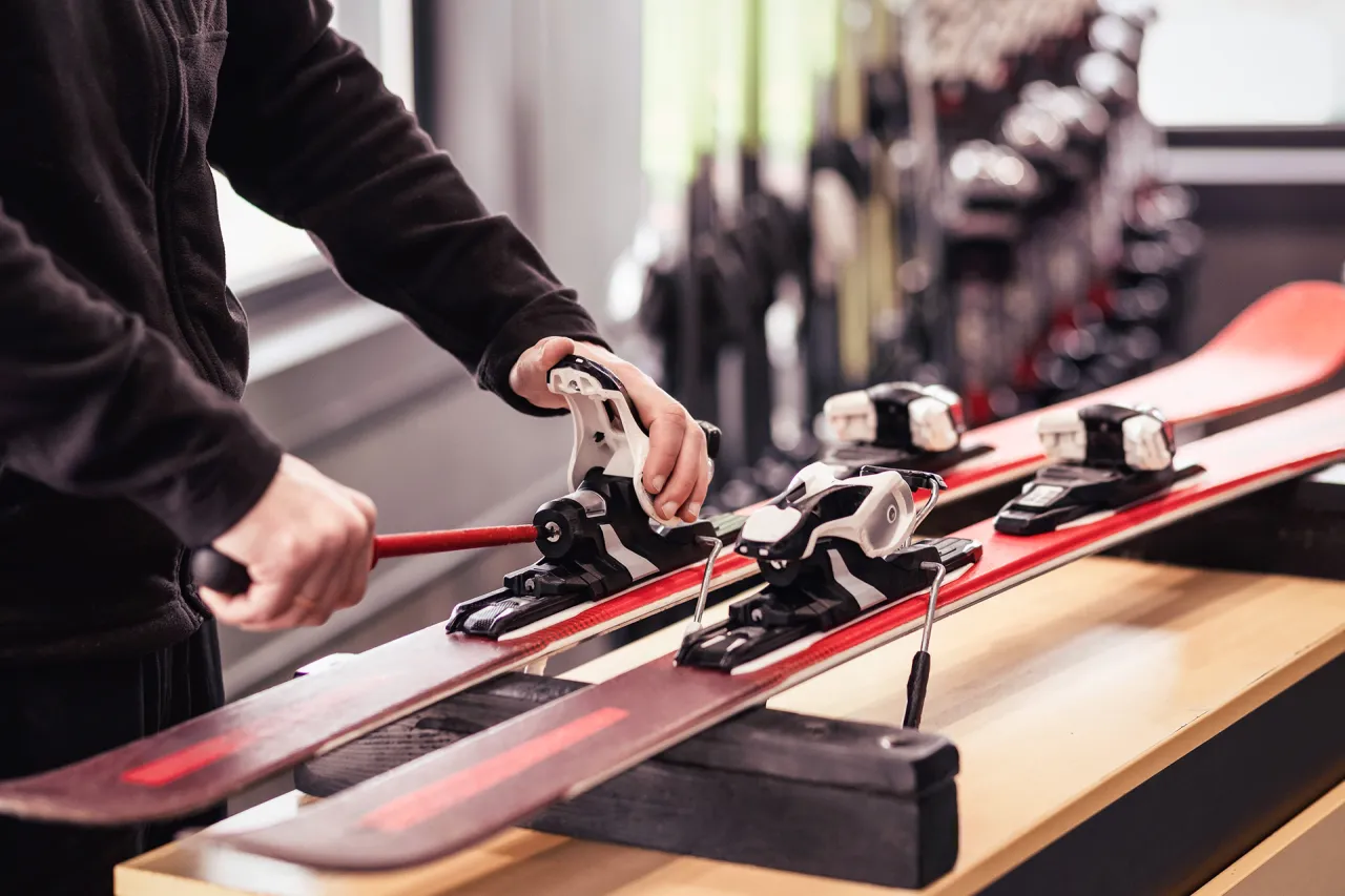 Dłoń reguluje siłę wypięcia wiązań narciarskich za pomocą narzędzia.