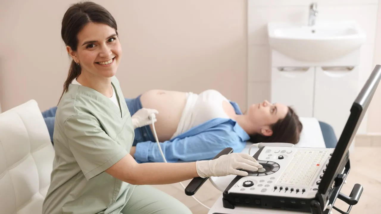 Lekarka wykonuje badania prenatalne, przygotowując przyszłą mamę do USG. Uśmiechnięta specjalistka z aparaturą USG.