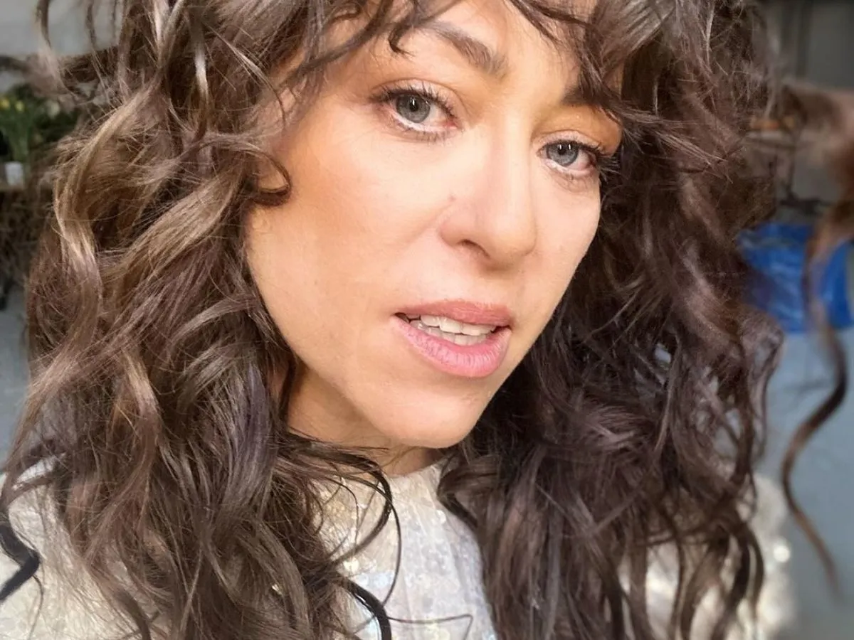 Kobieta z burzą brązowych, kręconych włosów. Wygląda, jakby właśnie dowiedziała się, jak zrobić mokrą włoszkę.