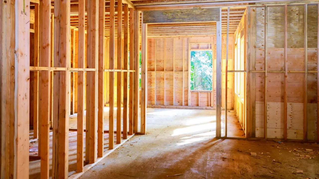Wnętrze domu szkieletowego w budowie. Drewniane belki tworzą ściany i stropy. Okno w tle wpuszcza światło. Ile lat przetrwa taki dom?