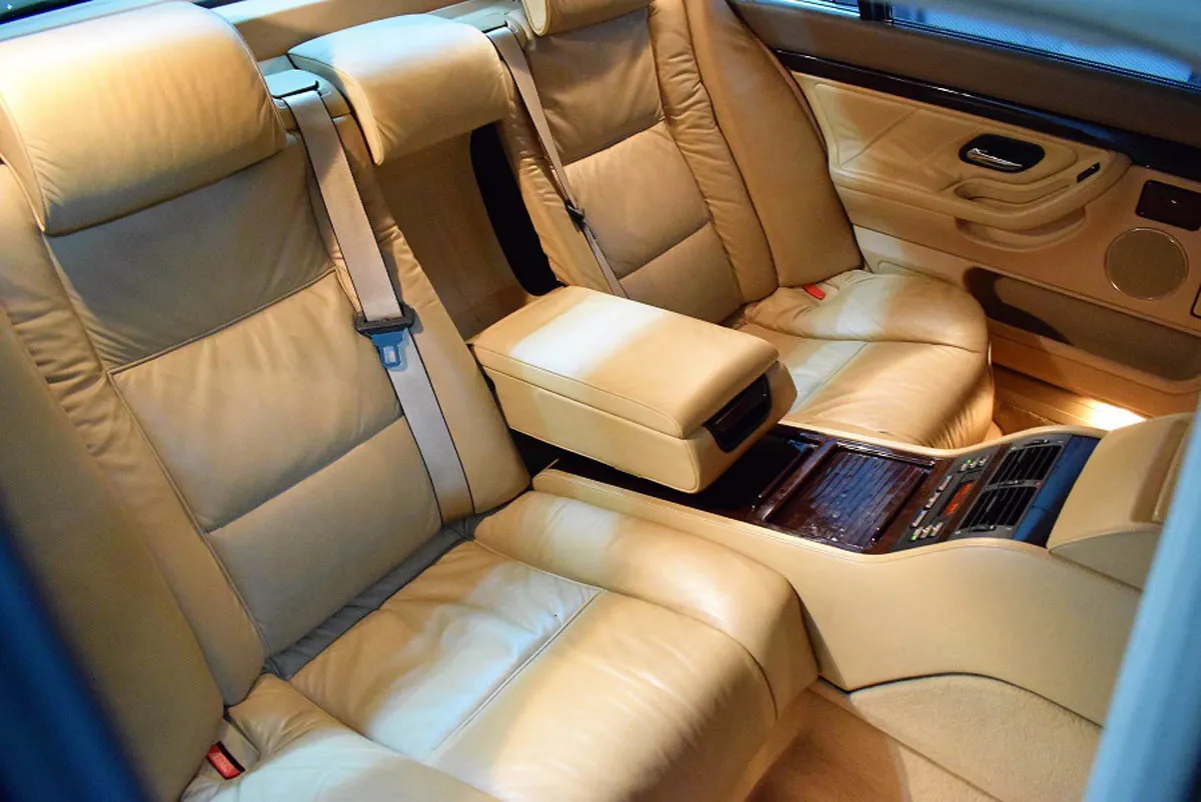 Wnętrze BMW E38 long z jasną, sk&oacute;rzaną tapicerką. Widoczne tylne siedzenia, podłokietnik i konsola środkowa.