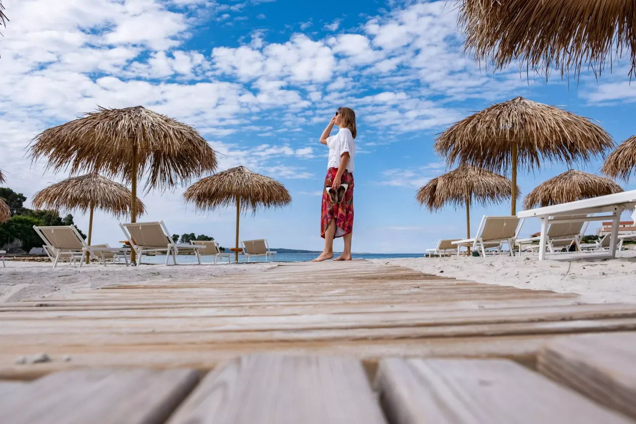 Kobieta na plaży na wyspie Rab, pod słomianymi parasolami, z widokiem na morze.