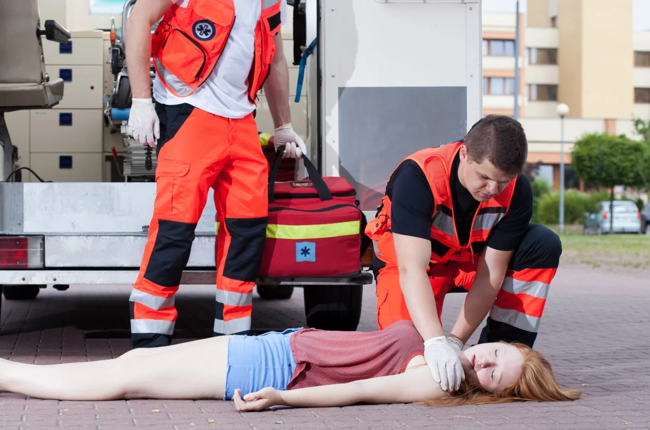 ratownik medyczny udzielający pomocy, inna osoba stoi z boku