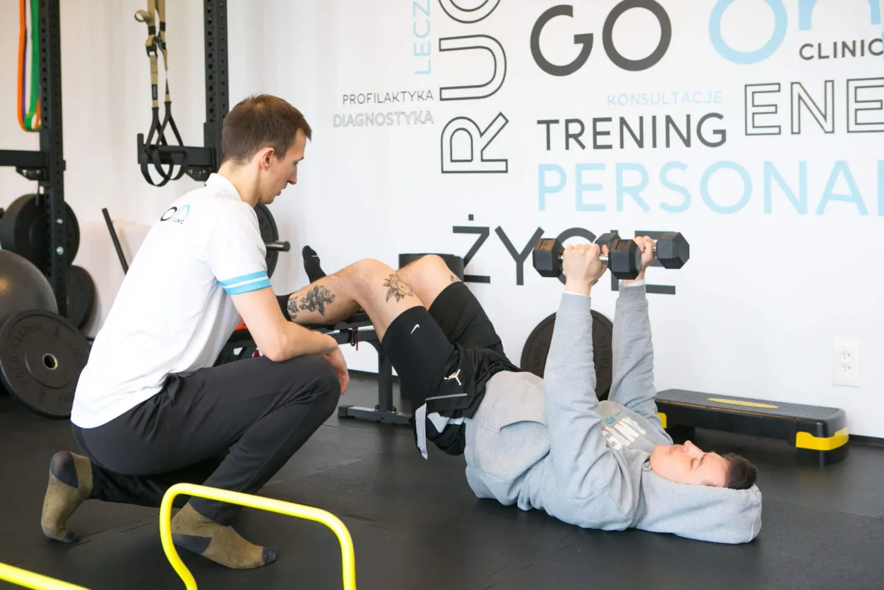 Fizjoterapeuta nadzoruje ćwiczenia z hantlami. To przykład, co to jest fizjoterapia: rehabilitacja i trening.