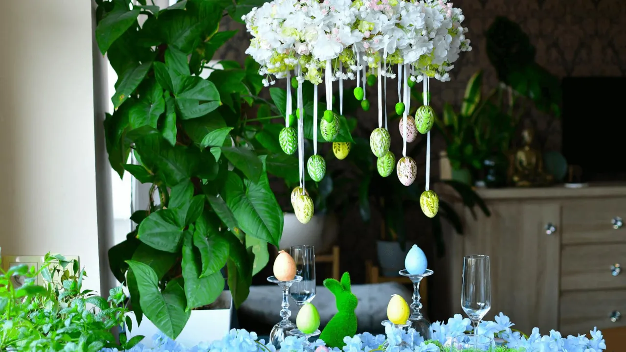Jak zrobić stroik wielkanocny: wiszące pisanki, zielony zajączek i kwiaty tworzą wiosenną dekorację stołu.