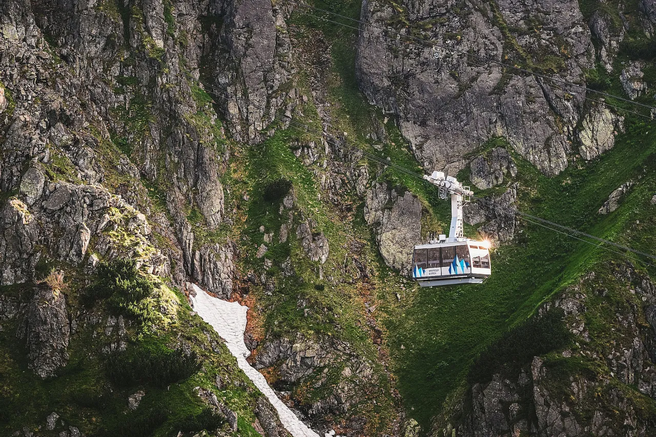 Kolejka linowa PKL Kasprowy Wierch wspina się po skalistym zboczu Tatr, mijając resztki śniegu i soczystą zieleń.