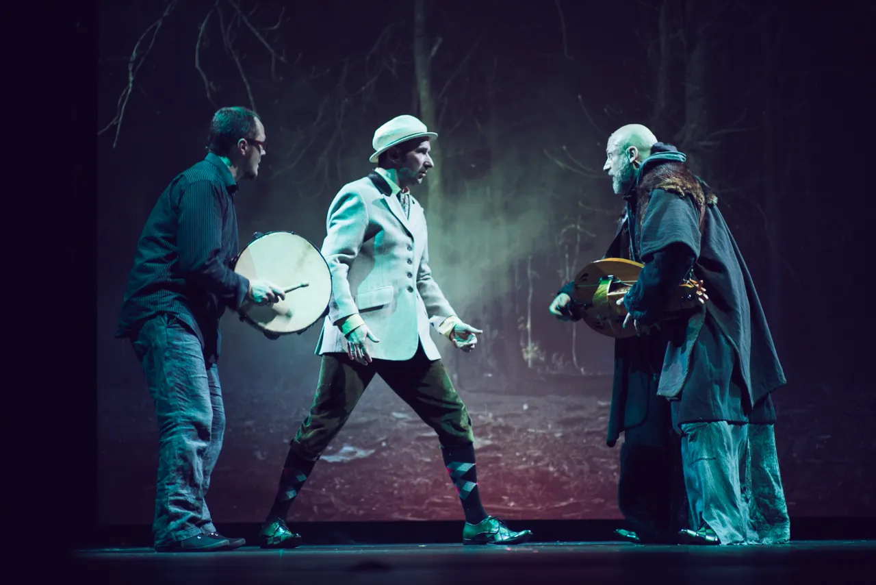 Trzech mężczyzn na scenie. Jeden gra na bębnie, drugi w białym kapeluszu i marynarce, trzeci w stroju z futrem, gra na lirze korbowej. To skład kabaretu Mumio.